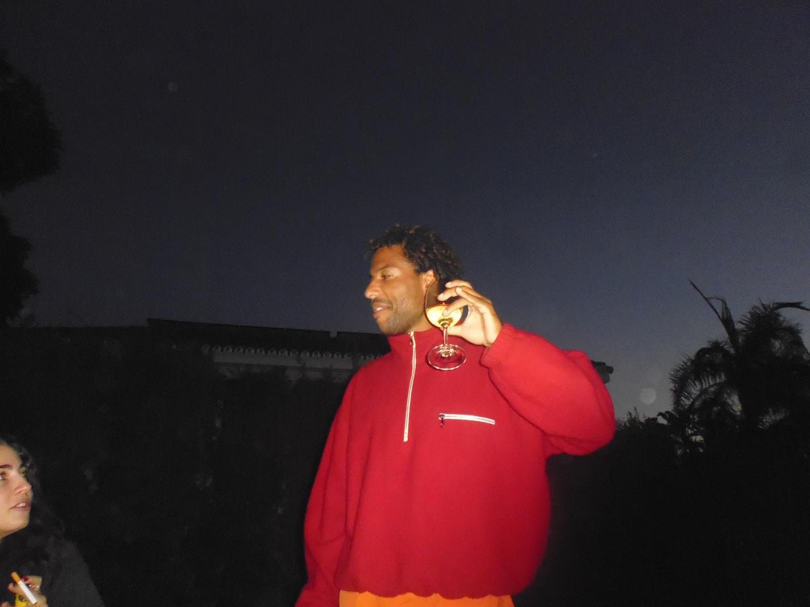 A bright red oversized half-zip fleece is worn over orange bottoms in a dark outdoor setting.
