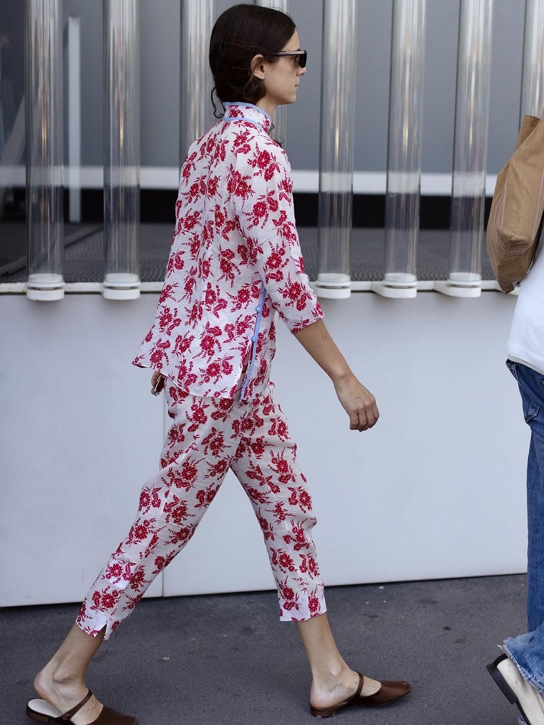 A white matching floral set with red print is styled with dark sunglasses and brown low-heeled mules.