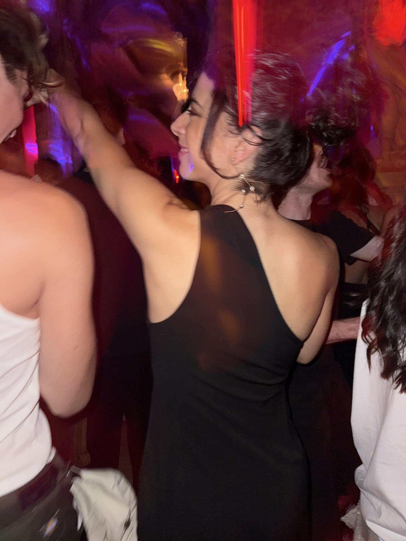 A fitted black sleeveless open-back dress is styled with delicate dangling earrings and an undone updo.