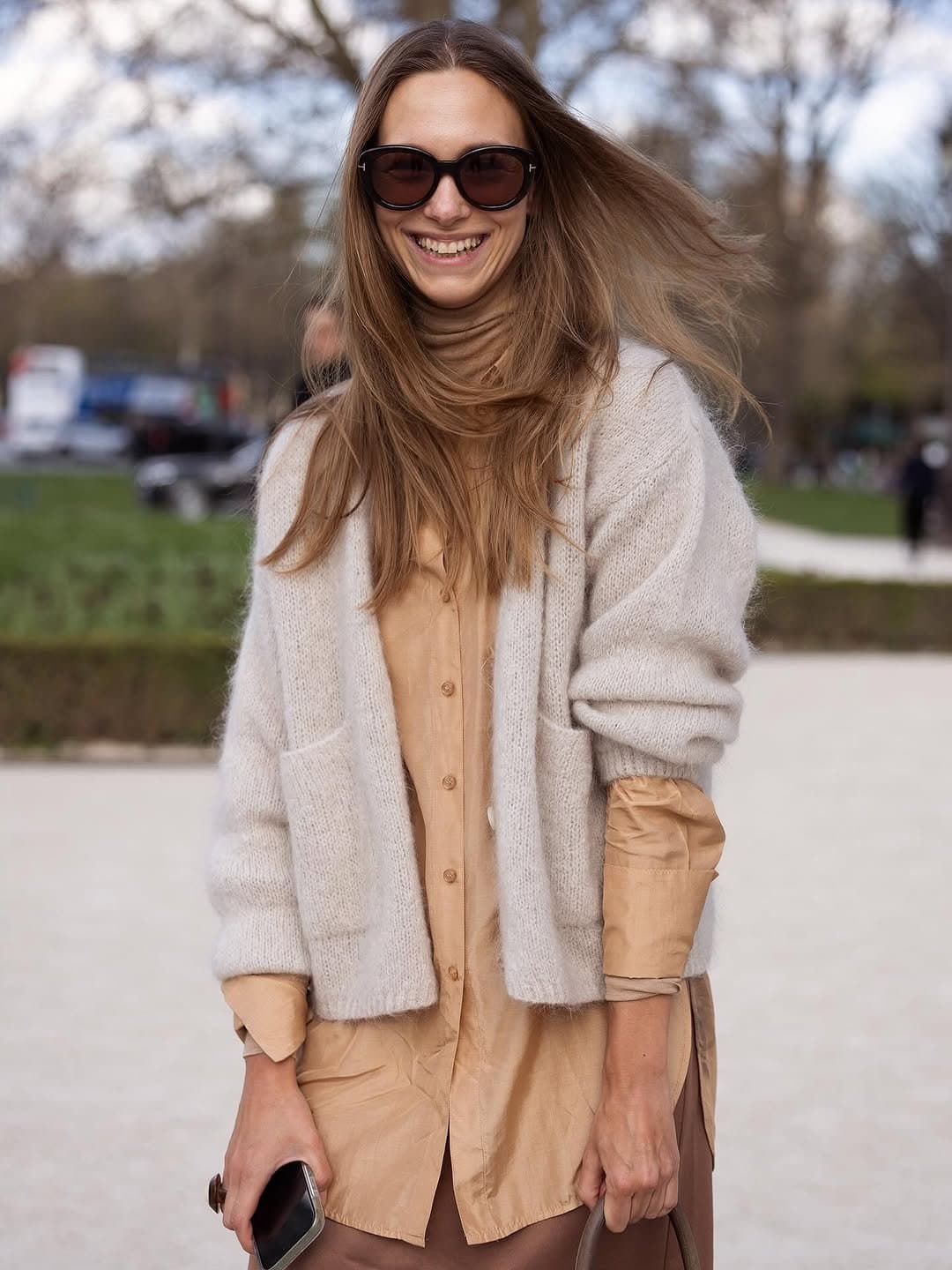 A camel button-up shirtdress is layered under a soft light grey oversized cardigan with dark rounded sunglasses.
