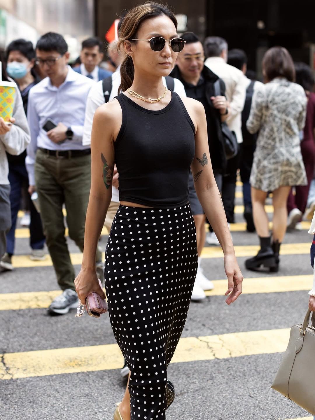 Ipinareha ang fitted na itim na tank top sa midi skirt na mataas ang baywang at may itim-at-puting polka dot pattern, bilog na sunglasses, alahas na ginto, at maliit na pink na clutch.