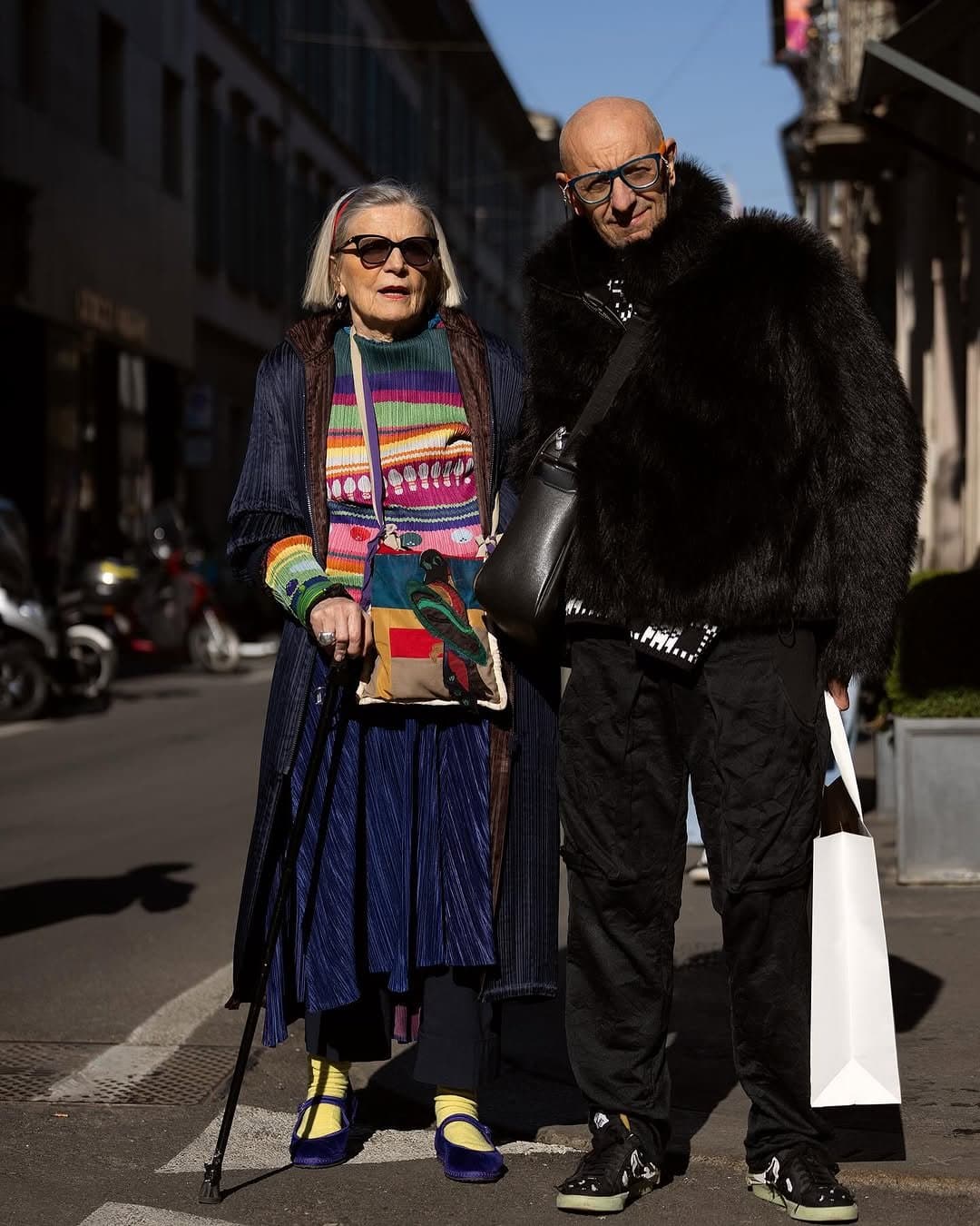 Two street-style looks pair a colorful layered knit and pleated skirt with a black faux-fur outerwear look and cargo trousers.
