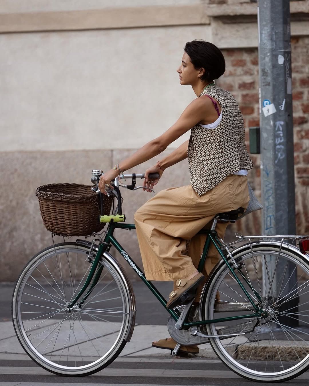 A sleeveless patterned vest is layered over a white tank with tan wide-leg cropped trousers and buckled tan sandals.