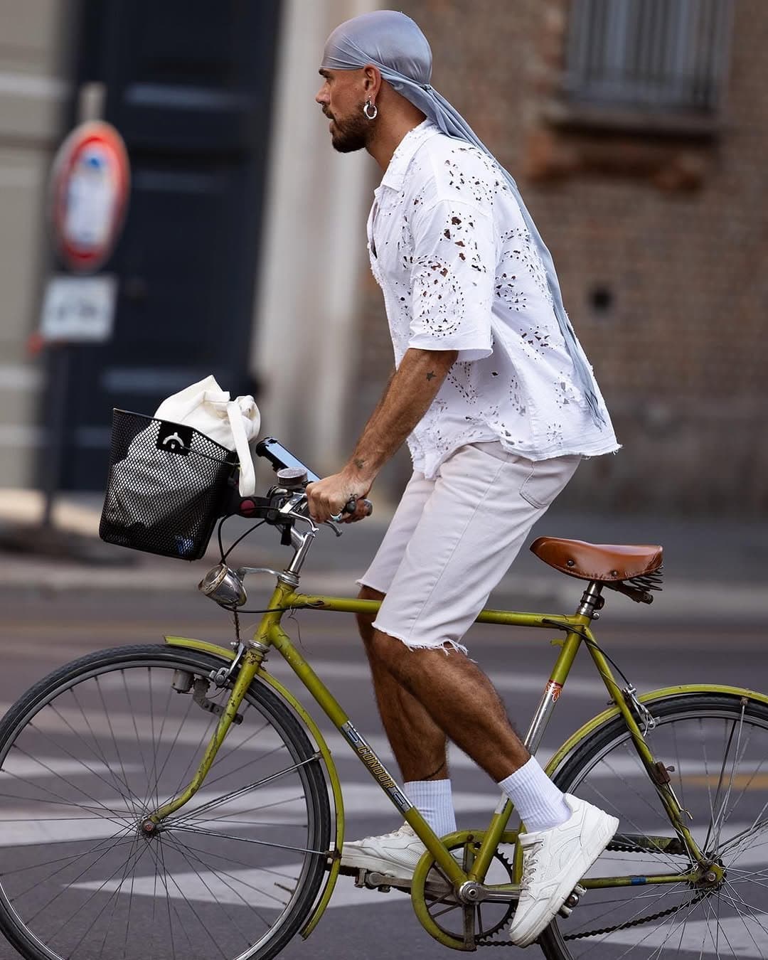 A white eyelet short-sleeve shirt and white cutoff shorts are styled with a pale grey-blue headscarf, crew socks, chunky white sneakers, and silver jewelry.