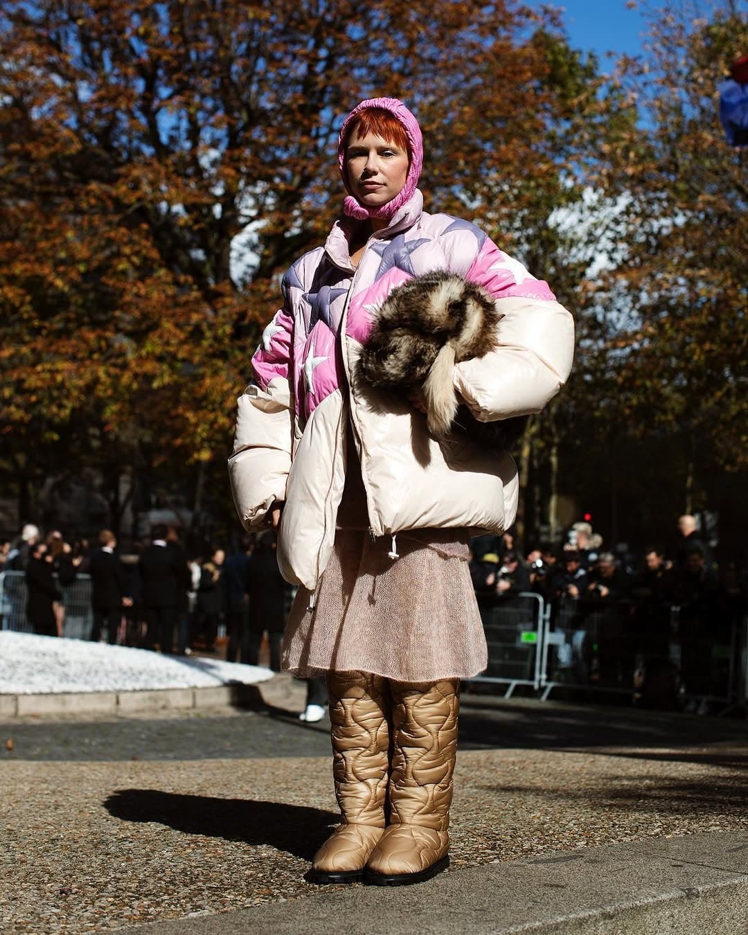A pastel oversized puffer jacket is styled with a pink tied headscarf, short textured skirt, quilted gold boots, and a plush fur-like hand accessory.