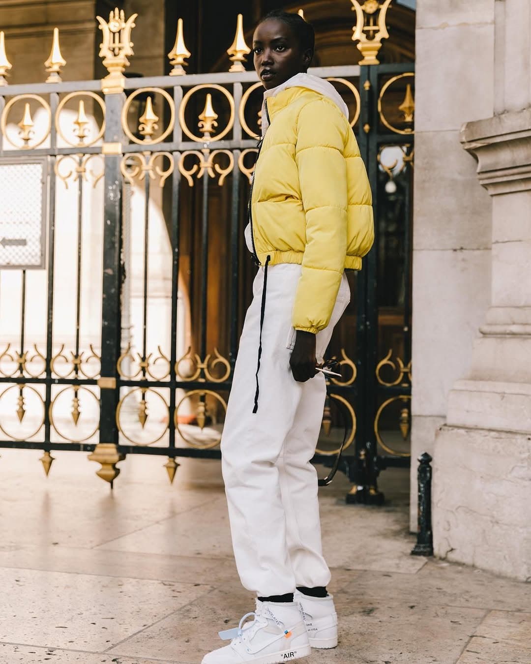 A pale yellow cropped puffer is layered over white sweats and white high-top sneakers with black accent details.