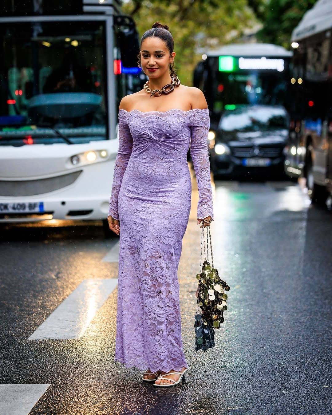 Lavender off-shoulder lace maxi dress styled with a chunky chain necklace, embellished chain bag, and white strappy heels.