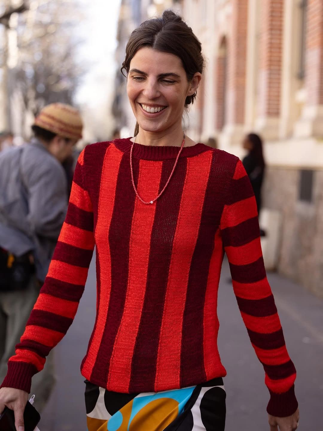 A fitted red and burgundy striped knit sweater is paired with an abstract multicolor printed skirt and delicate beaded jewelry.