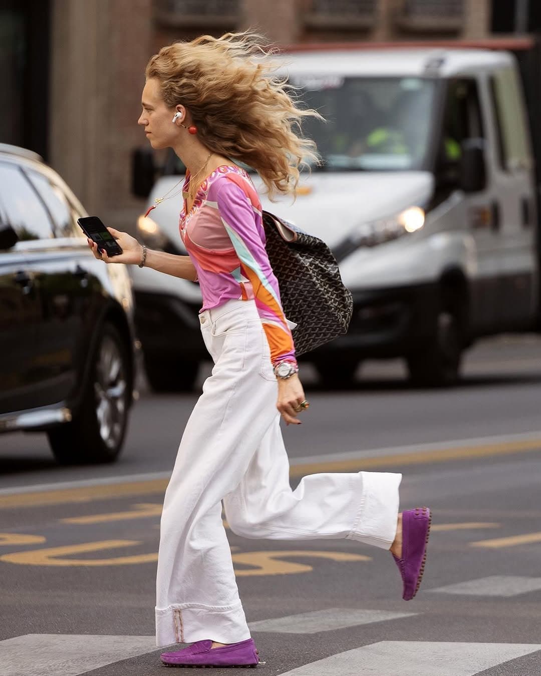 A colorful fitted printed top is styled with white wide-leg trousers, purple loafers, and a large black woven shoulder bag.